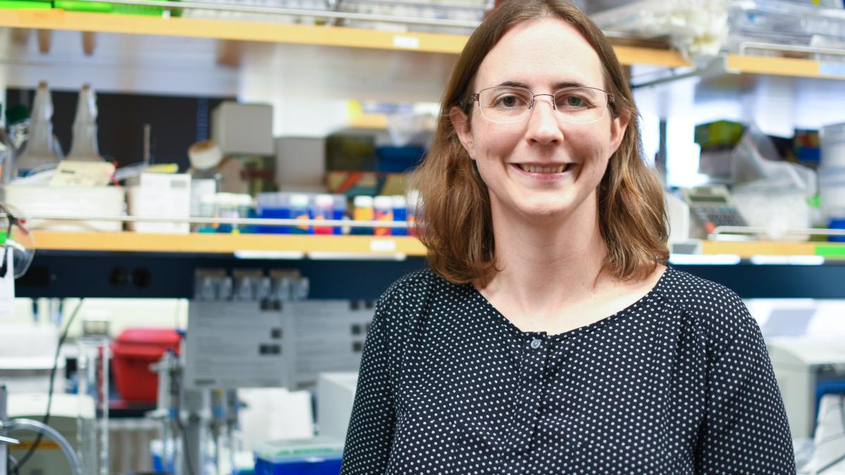 Ashleigh Theberge stands in front of shelves crammed with lab equpiment and supplies. 