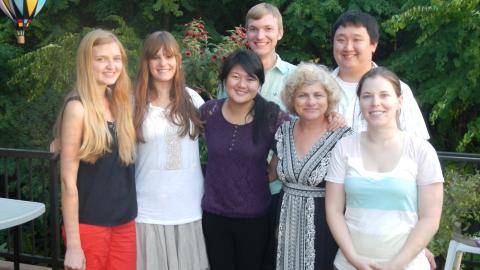 A group of six students stand with Professor Roberts on a deck with trees in the background.