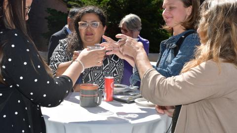 A group of women stand around an outdoor table making a toast