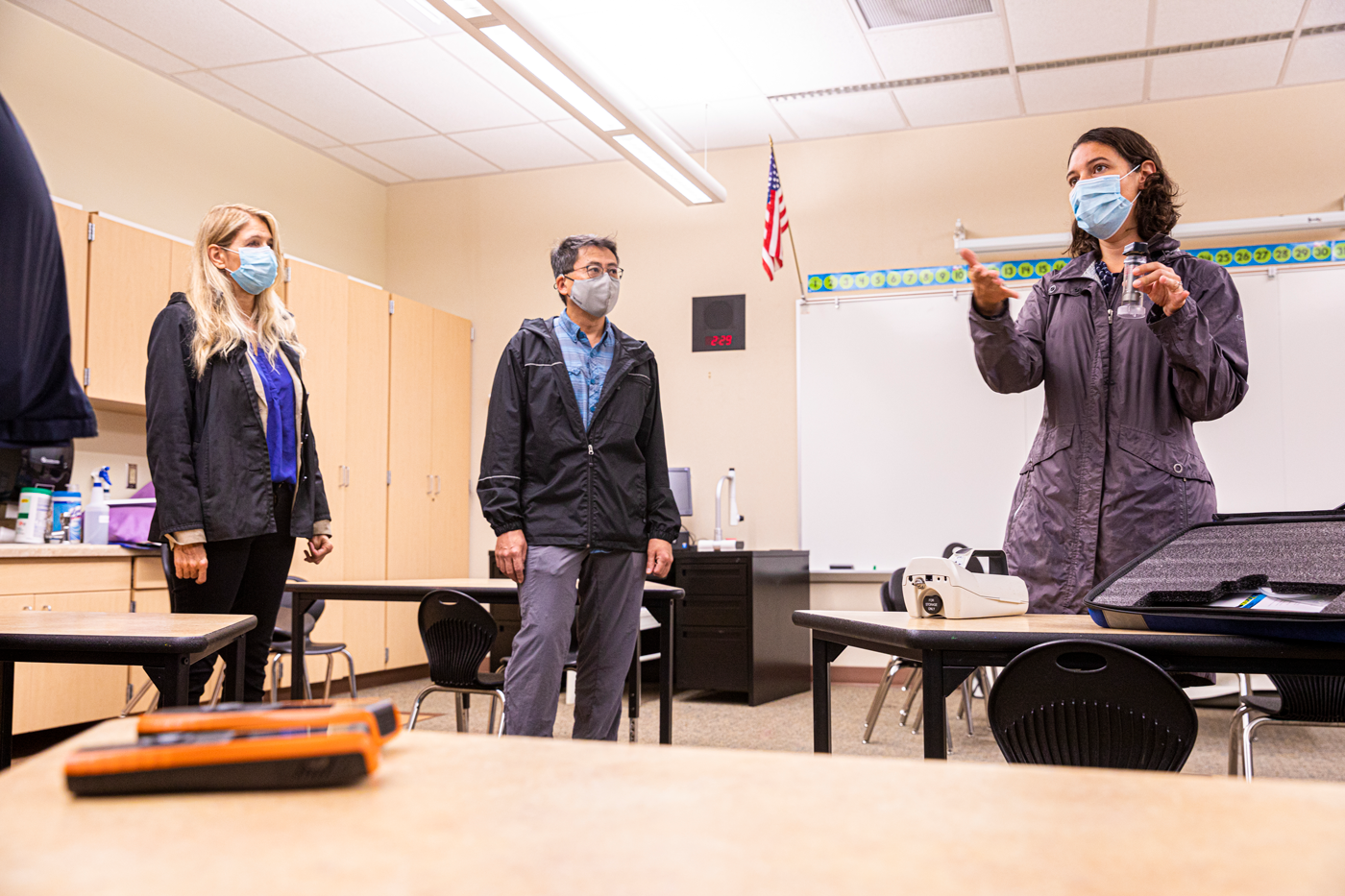 Three people stand in a classroom. At right, Professor Elena Austin demonstrates air monitoring methods.