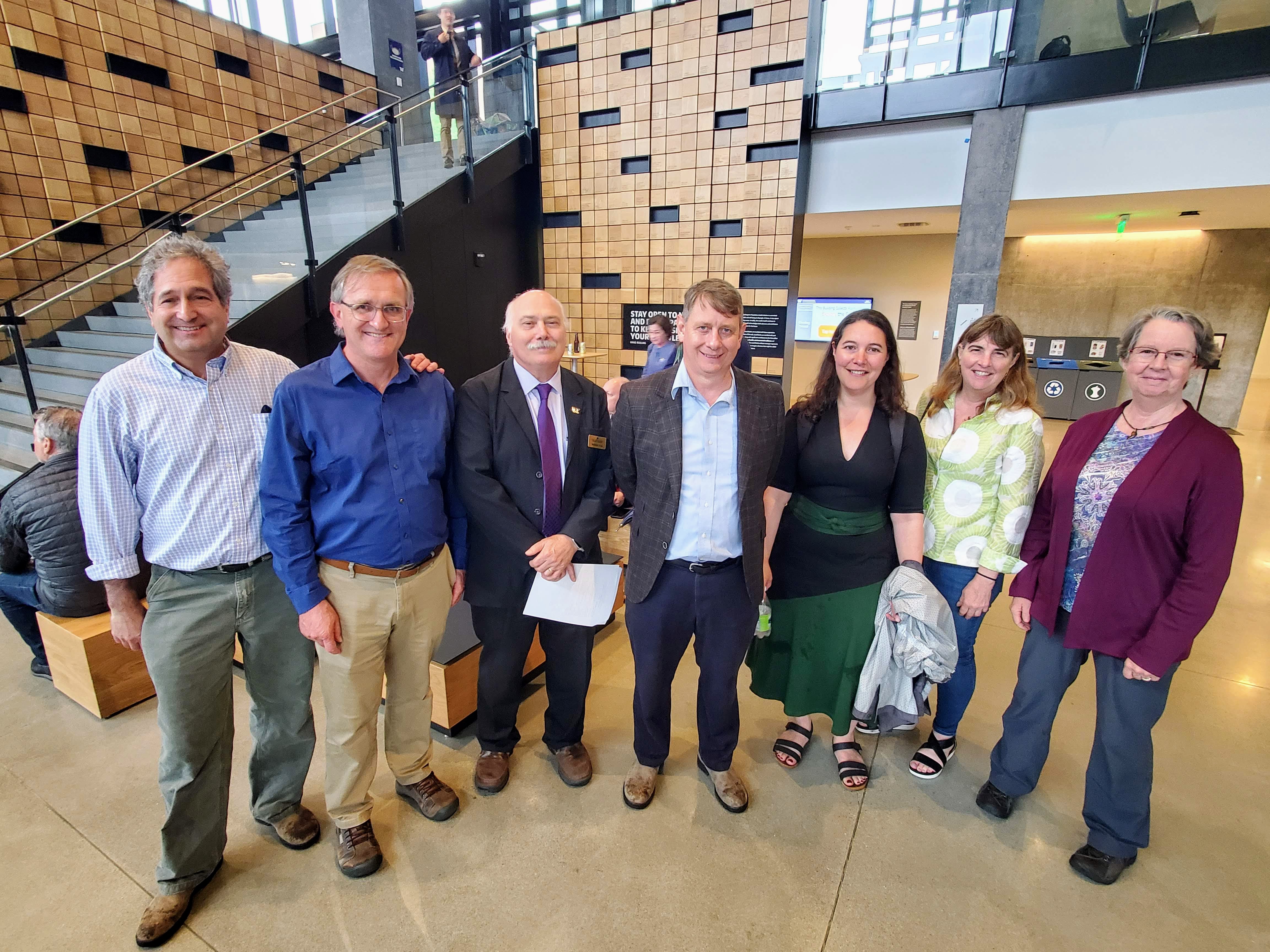 A group of faculty stand in a half-circle in a large atrium.