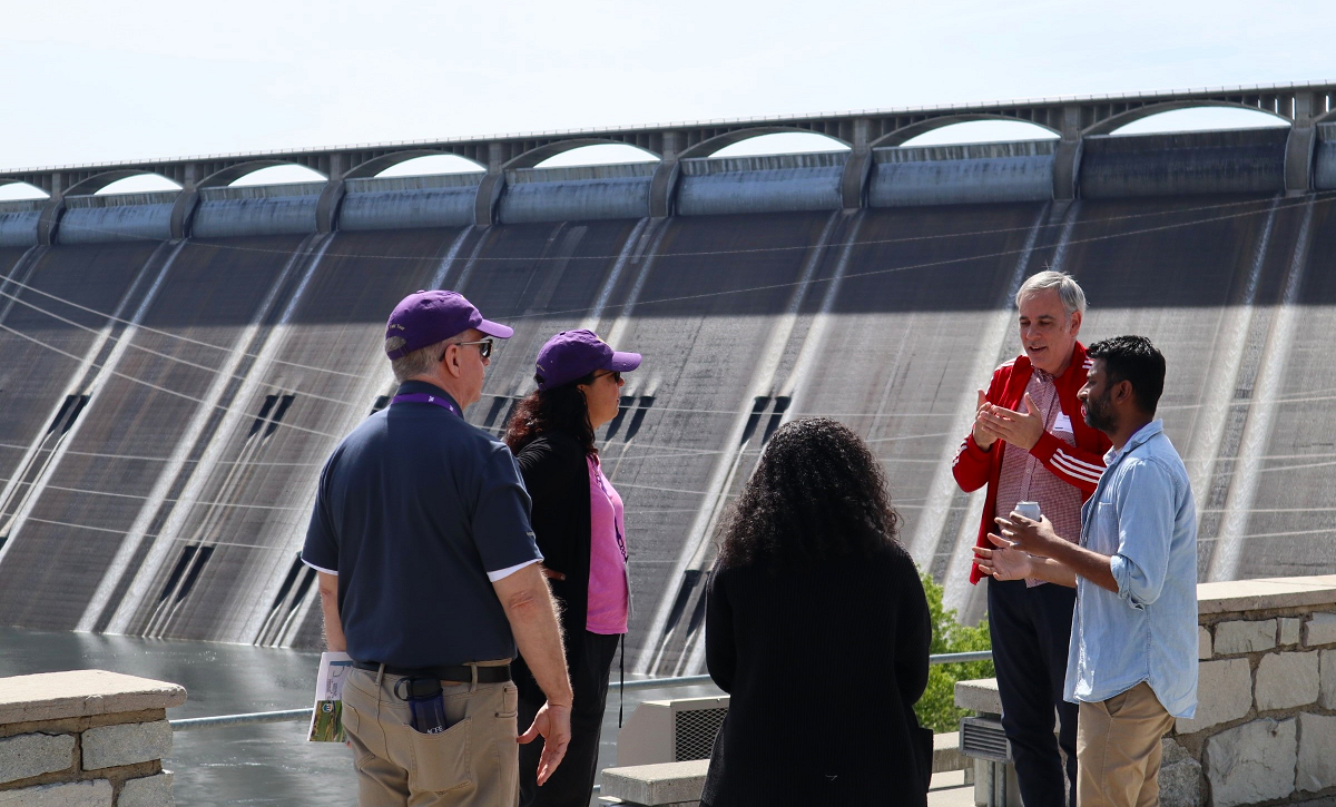 Five people stand talking in front of the Grand Coulee Dam.