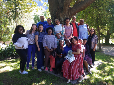 14 people stand together in a group photo under a tree.