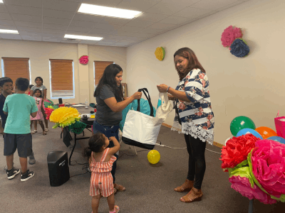 A woman receives a bag of air quality resources from another woman with children playing in the background.