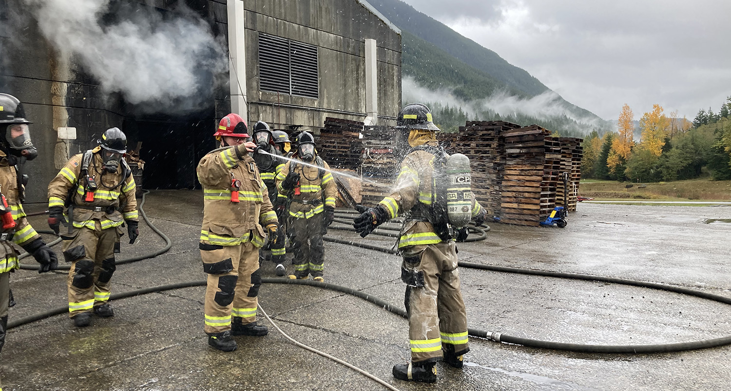 One firefighter hoses another down during a training exercise as several other firefighters look on.