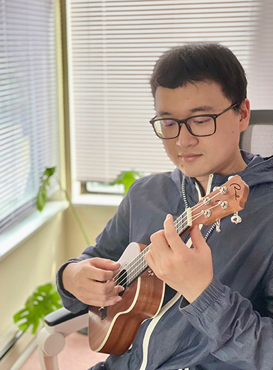 Man sitting in a chair playing ukulele.