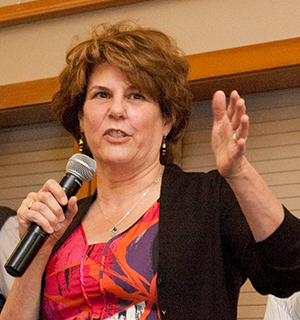 A woman standing with a microphone speaking to an audience.