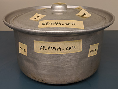 An aluminum cookpot with yellow labels on it.