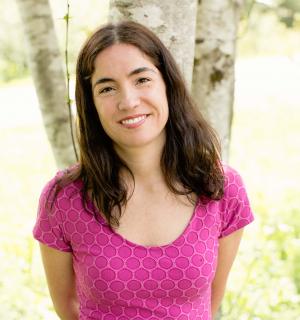 A woman smiles standing by a tree