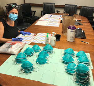 Codsi, wearing a face mask and gloves, sits at a table with N95 masks and papers. 