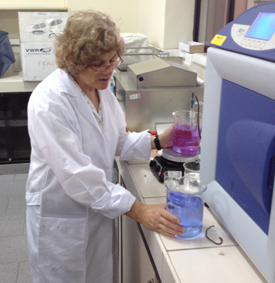 Professor Roberts, wearing a lab coat and glasses, in a lab holding onto two beakers, one with purple liquid and one with blue liquid.