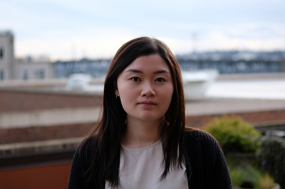 Shirley Huang stands on a roof with a bridge in background.