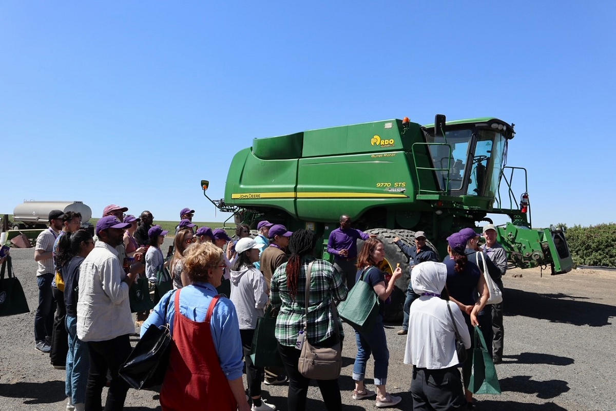 A group of about 30 people stand in front of a giant farming machine.