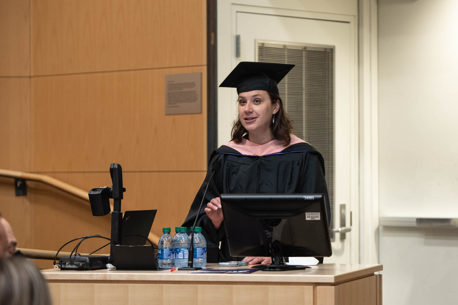 A student in cap and gown speaks at a podium.