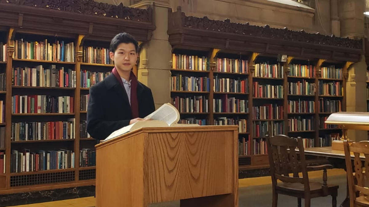 A man in a coat stands at a podium in a library.