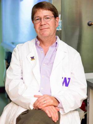 Headshot of Edward Kelly, a middle-aged white man with brown hair and glasses, wearing a lab coat