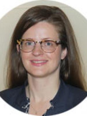 Headshot of Katrin Burkart, a young white woman with tortoiseshell glasses and long brown hair