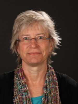 An older white woman with short fluffy gray hair, glasses, and a colorful scarf