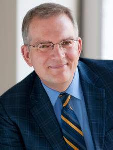 Dr Lewandoski, a middle aged white man with gray hair and small glasses, wearing a plaid navy suit