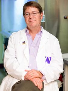 Headshot of Edward Kelly, a middle-aged white man with brown hair and glasses, wearing a lab coat