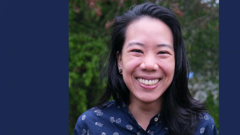 Close-up photo of Megumi Matsushita smiling outside in front of a bush.