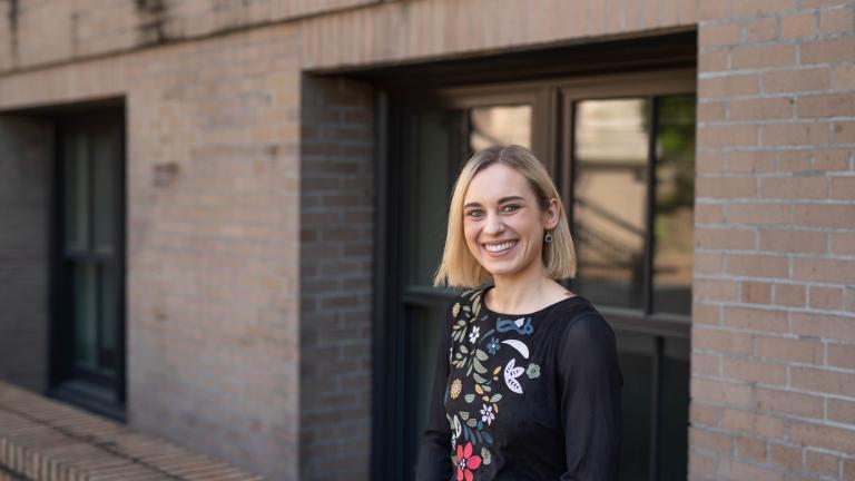 Asheton Gilbertson smiles in front of a window of a brick building on UW campus.