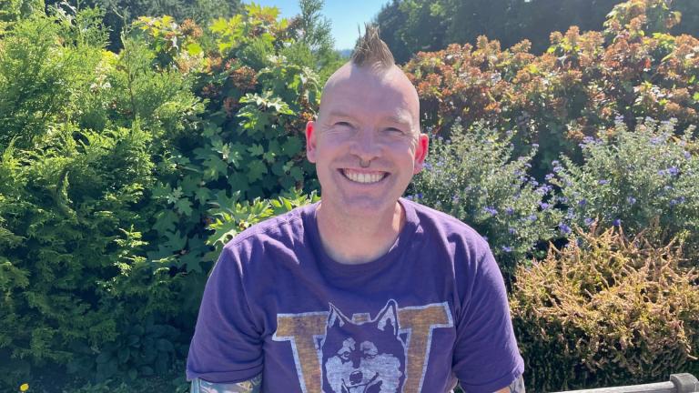 John Lykins smiles outside with a UW Huskies shirt on, in front of some bushes on the UW campus.