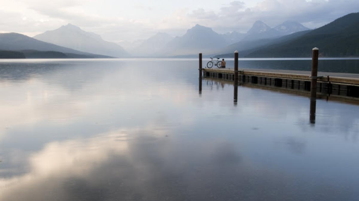 Dock, with person and bike on it over scenic lake with mountains in the background