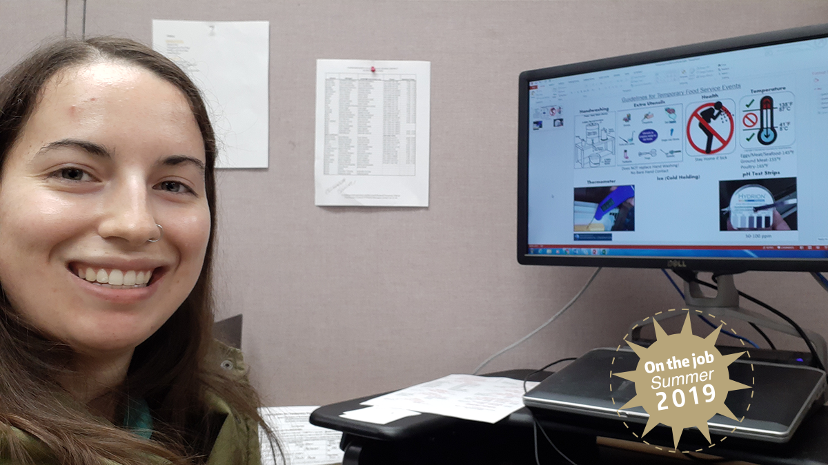 A woman smiles as she sits next to a computer monitor.