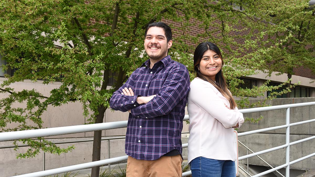 Two people stand back to back smiling at the camera.