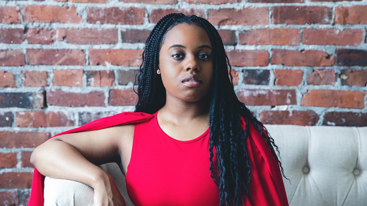 Portrait of woman dressed in red, sitting in front of a brick wall.