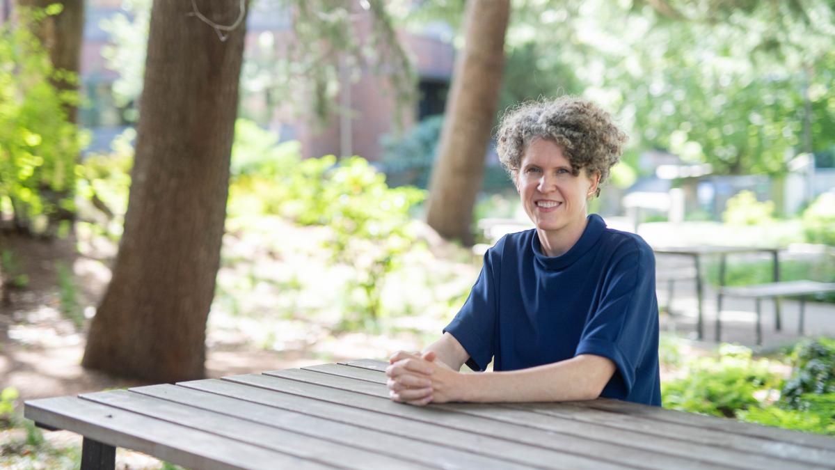 Joan Casey sits at a wood table outside on the UW campus with trees in the background.