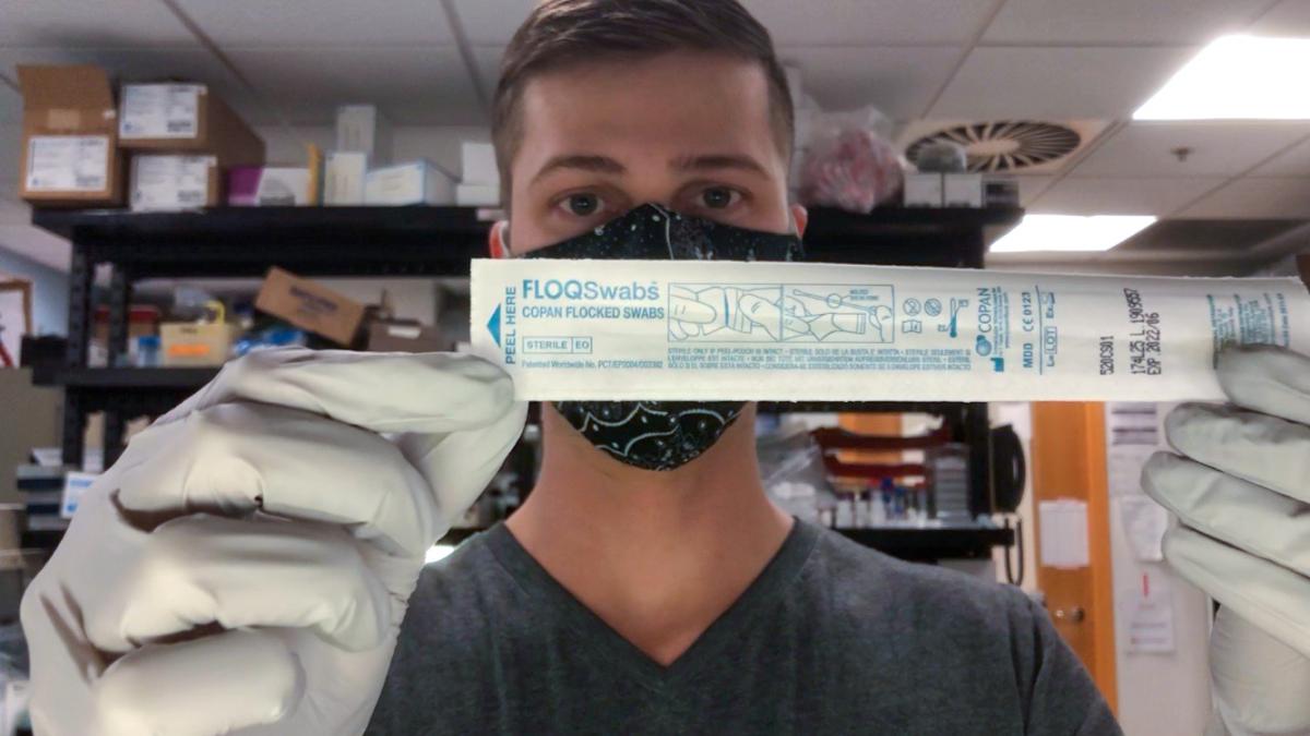 A man stands in a lab holding a swab in its paper packaging.