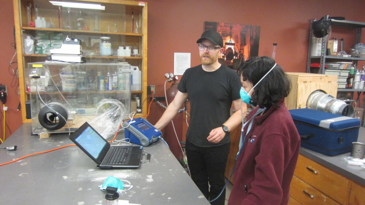 A man tests the fit of a face mask being modeled by a student.