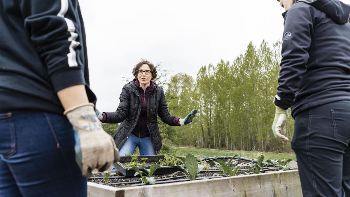 UW Lecturer Yona Sipos gestures to students standing near raised gardening beds at the UW Farm.ities of food systems through hands-on activities at the UW Farm. Photo: Elizar Mercado.