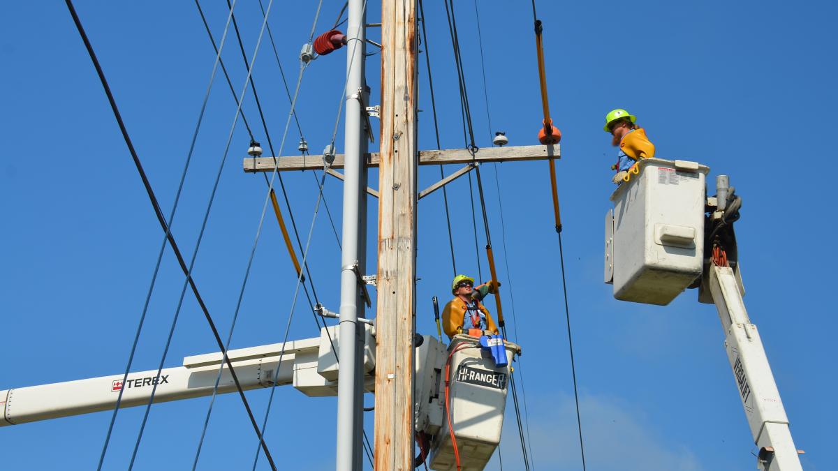 Utility workers in cherry pickers work on electrical power lines.