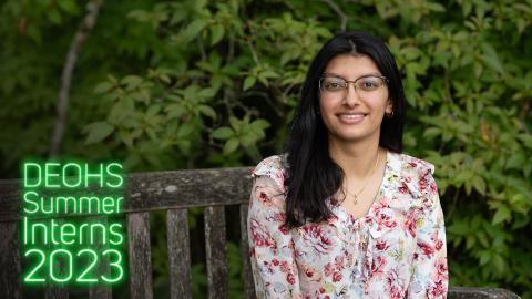 Anika Rajput sits on a bench on the UW campus with greenery in the background.