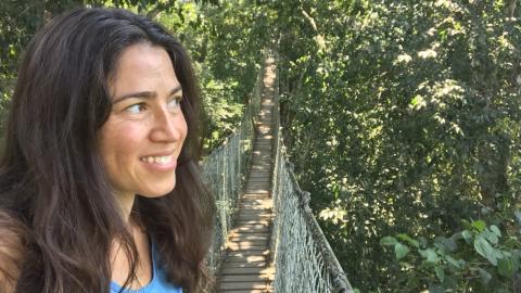 Woman looking to the right with a rope and wood bridge behind her in a forested landscape.