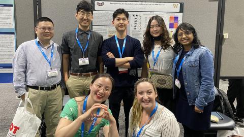 A group of seven researchers stand in front of a poster.