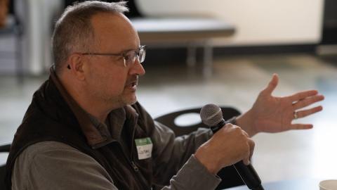 Closeup of Dr. Jeremy Hess in profile holding a microphone with one hand and holding out his other hand.