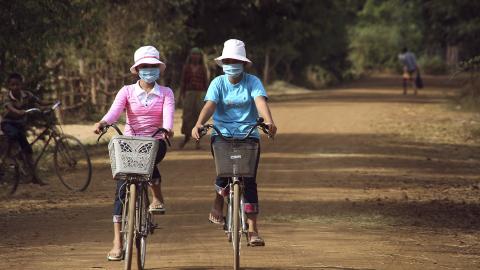 Two women wearing air masks on bicycles on a dirt road.