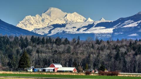 A red barn and farmland in the foreground with Mount Baker in the background.