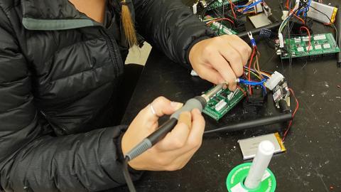 Close up of UW student Natalia Kowalchuk's hands holding a soldering iron as she builds an air monitor in a lab. Photo: Kayla Cayton.