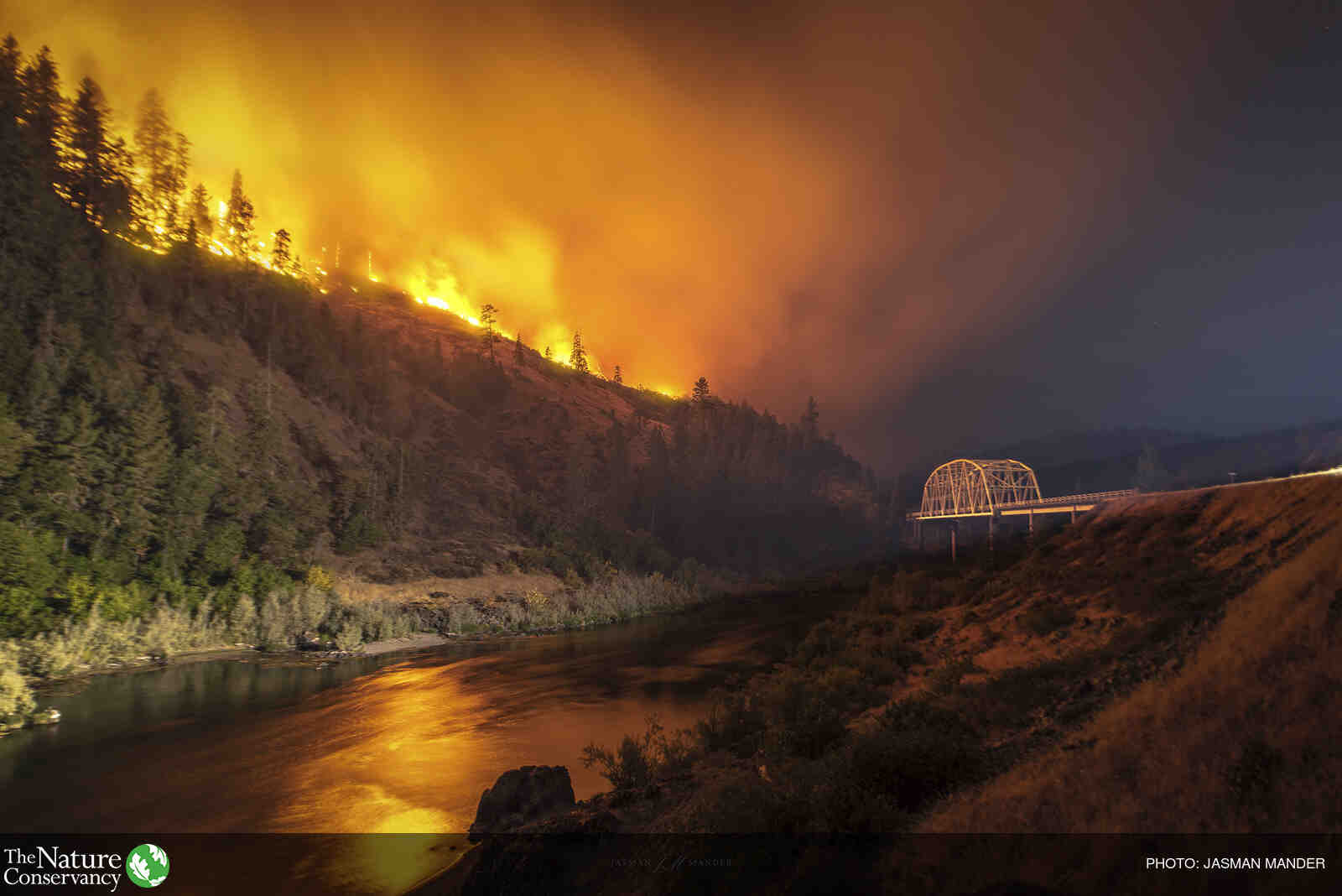 Wildfire on a ridge above a river and bridge.